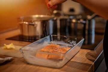 Female hand sprinkles spices on grilled salmon in a cast glass grilling pan. Stir fried salmon in the pan.