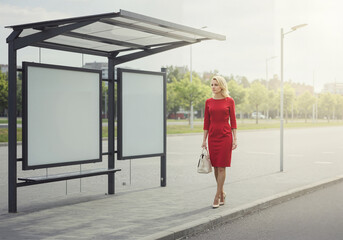 Confident woman in red dress walking towards bus stop in sunlight  