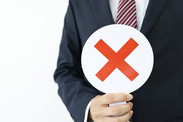 スーツ男性が赤いバツ印の札を持つ否定や禁止のイメージ