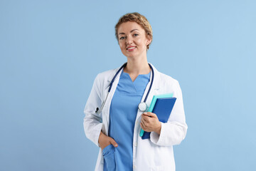 Portrait of professional pediatrician with stethoscope and notebooks on light blue background