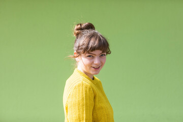 Young woman in yellow sweater smiles in front of a bright green background. Germany