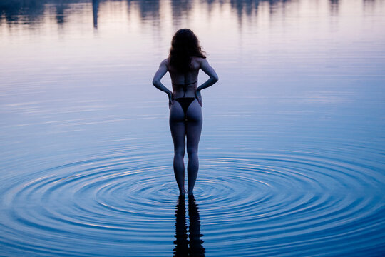 Woman in swimwear standing in calm water with gentle ripples at sunset. WA, USA