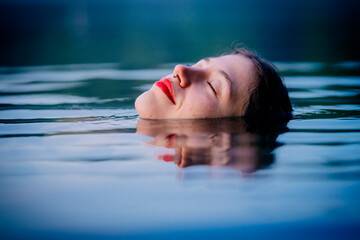 A woman with closed eyes floats peacefully on water with a serene expression. WA, USA