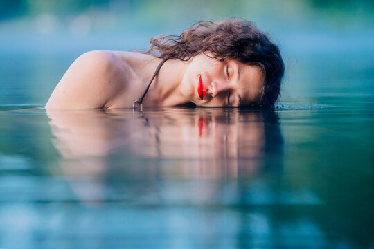 Woman with curly hair partially submerged in water, resting her head sideways on surface. WA, USA