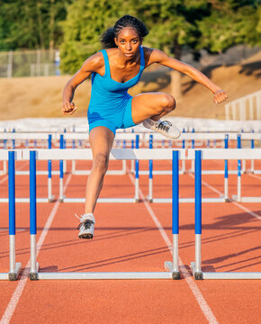 Athlete in blue jumpsuit clears hurdle on a sunny outdoor track. USA