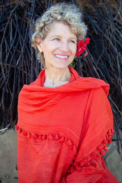 Smiling mature adult in red wrap with floral accessory against a rustic twig backdrop.  Kepaniwai Park, Wailuku, Hawaii