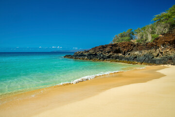 Pristine beach with turquoise waters, golden sand, and rocky cliff under a clear blue sky. Makena, Makena state park, Oneloa beach, Maui, Hawaii