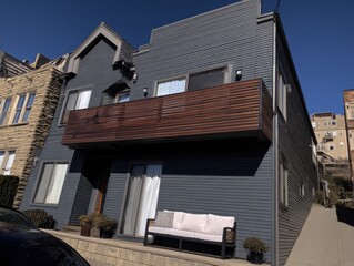 A large, modern house with a balcony and a white couch on the front porch. The house is surrounded by trees and has a very clean and minimalist appearance
