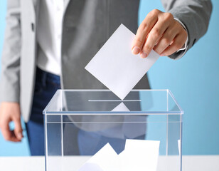 una mano de hombre metiendo una papeleta en una urna de cristal transparente en una votación para elecciones libres en democracia con voto ciudadano, participación y transparencia electoral