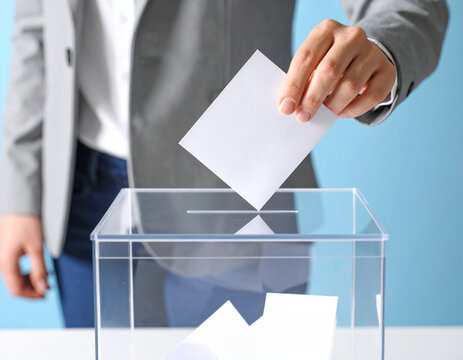 una mano de hombre metiendo una papeleta en una urna de cristal transparente en una votaci&oacute;n para elecciones libres en democracia con voto ciudadano, participaci&oacute;n y transparencia electoral