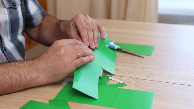 Hands folding and gluing cardboard cutouts, assembling parts of paper model for creative DIY craft project.