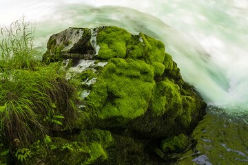 white rock covered with moss on flowing stream background. abstract nature background. minimalist rocky background with a flowing stream. artistic
