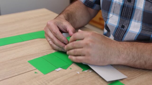 Hands folding and gluing cardboard cutouts, assembling parts of paper model for creative DIY craft project.