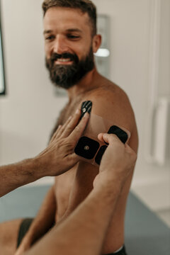 Physiotherapist applying electrodes on patient's shoulder for electrical muscle stimulation