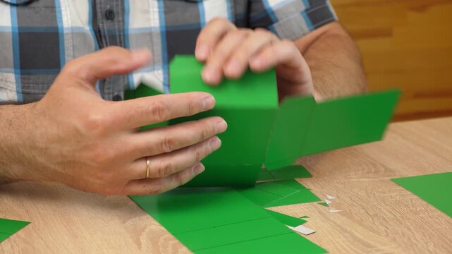 Hands folding and gluing cardboard cutouts, assembling parts of paper model for creative DIY craft project.