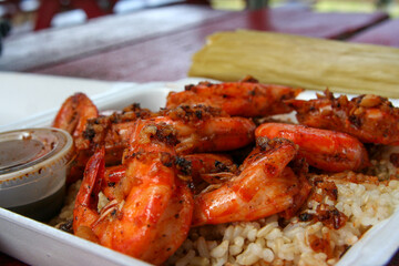 Garlic shrimp plate with rice and sauce in takeout container
