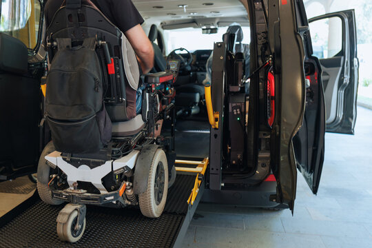 Person with disability operates a wheelchair lift to enter an accessible van parked outside, showcasing mobility solutions for improved access.