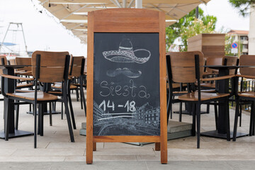 An empty restaurant features a chalkboard sign announcing siesta hours from 14 to 18, highlighting a quiet atmosphere in the afternoon.