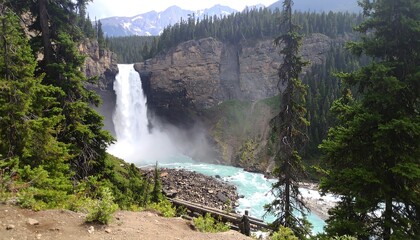 A breathtaking cascade of water tumbles down a rocky cliff face, surrounded by lush greenery and a vibrant blue river below.