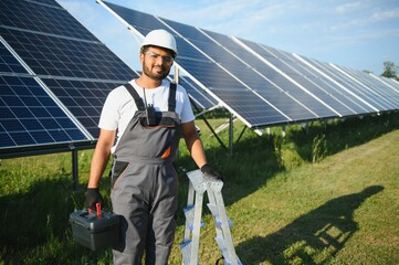 Indian man in uniform on solar farm. Competent energy engineer controlling work of photovoltaic cells