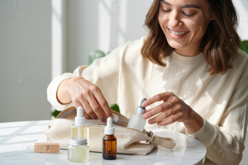 Smiling woman happily organizing her favorite skincare products and serums from a chic makeup bag, showcasing self-care routines and beauty essentials.