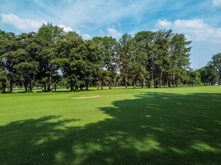 Obraz premium Golf course with green grass field and trees under blue sky