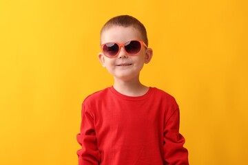 Cute little boy in sunglasses laughing on yellow background