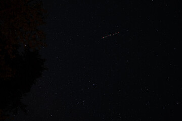 Dark night sky full of stars with airplane light trail captured in long exposure, astrophotography scene.