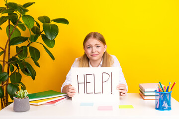Worried girl holding help sign at school desk expressing stress in bright classroom setting with school supplies