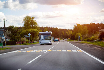 Fototapeta premium A suburban bus carries passengers along a road in a village against the backdrop of sunset. Copy space for text, traffic
