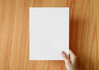 Fototapeta premium Hand holding blank paper on a wooden surface