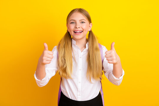Smiling schoolgirl in white shirt with thumbs up gesture on vibrant yellow background expressing happiness and positivity