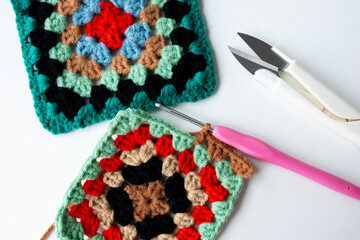 Contrast of colorful handmade crochet granny squares with hook and yarn scissors