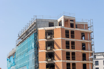 Construction site of modern brick apartment building with scaffolding and safety netting