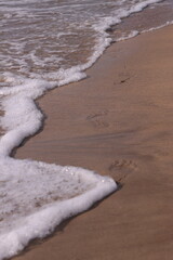Footprints in the sand near a sea wave