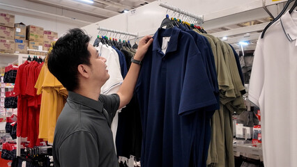 A man is looking at a rack of shirts in a store