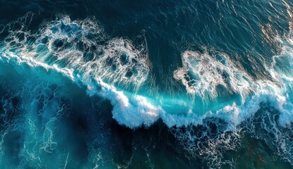Aerial view captures a cresting ocean wave, showing turquoise water transforming into white foam as it crashes