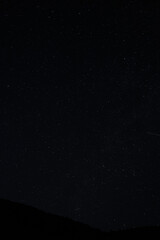 Night sky filled with stars above mountain ridges, peaceful astrophotography view of constellations.