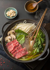 Hot pot with sliced beef, noodles, mushrooms, and fresh green vegetables steaming