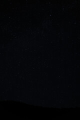 Night sky filled with stars above mountain ridges, peaceful astrophotography view of constellations.