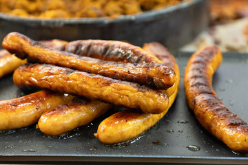 Grilled sausages stacked on a black plate with a blurred background of cooked food