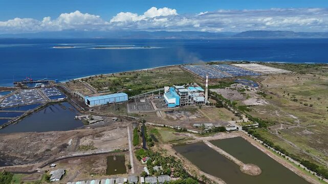 Aerial drone view of a coastal power plant operating next to traditional aquaculture shrimp farms, showing the coexistence of industry and local economy
