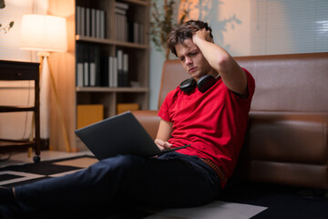 Fototapeta premium Young man touching his head and feeling tired and stressed from working on a laptop at home at night