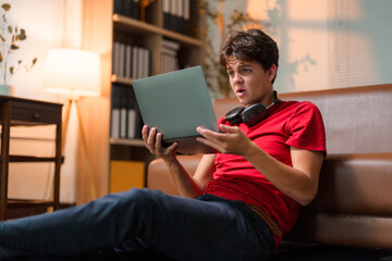 Young student video chatting from home, displaying shocked expression while looking at laptop screen