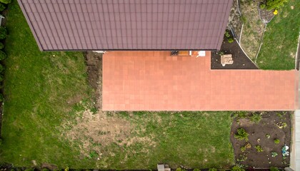 High-angle view of a terracotta-tiled patio area adjacent to a house with a brown roof, surrounded by lawns and gardens.