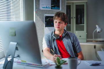 Student writing notes during virtual learning session, concentrated male working remotely on laptop computer