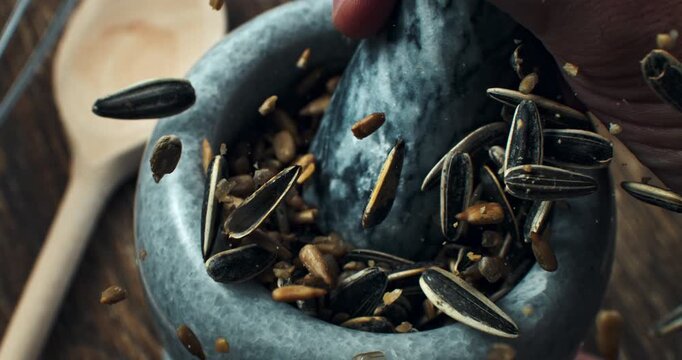 Slow Motion Close Up Of Sunflower Seeds In Stone Mortar With Pestle, Natural Organic Seeds, Healthy Ingredient For Cooking Baking Nutrition, Rustic Background With Wooden Spoon And Whole Seeds Texture