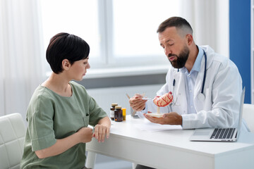 Gastroenterologist with model of stomach consulting woman in clinic