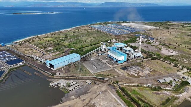 Aerial drone view of a coastal power plant operating next to traditional aquaculture shrimp farms, showing the coexistence of industry and local economy