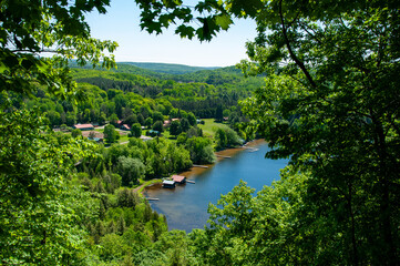 A breathtaking aerial shot captures a serene lake surrounded by lush greenery and scatterings of cozy houses, in a picturesque countryside during the summer season.